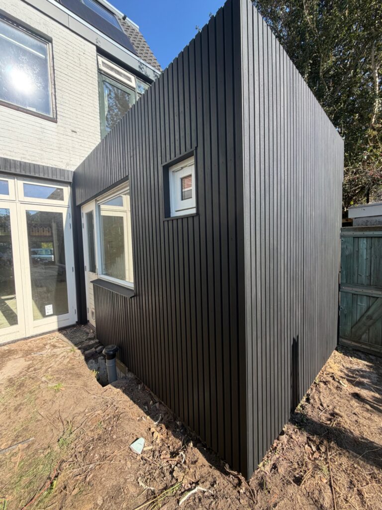 Uitbouw met zwarte verticale houten gevelbekleding en wit kozijn met klein raam
